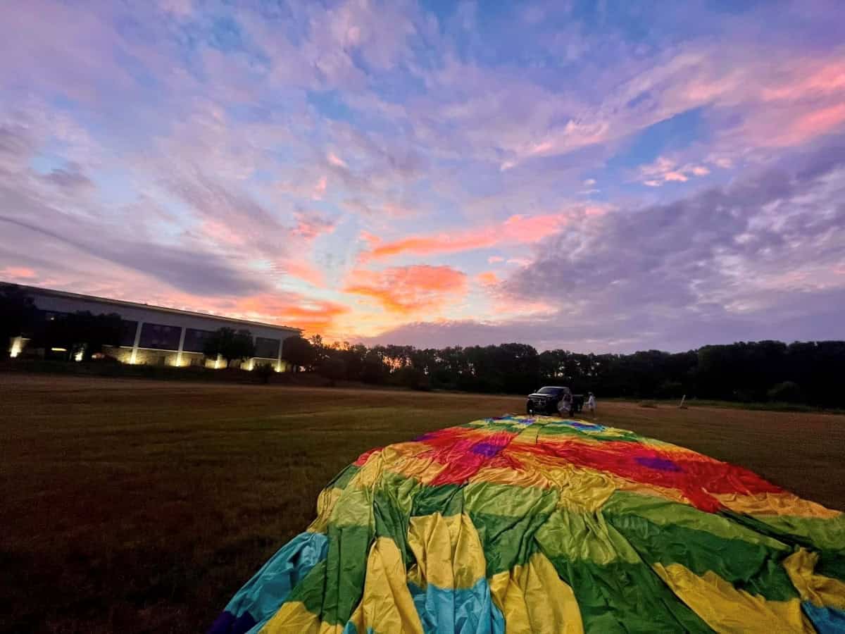 A colorful hot air balloon being prepared for takeoff at sunrise, representing the journey of becoming a hot air balloon pilot.